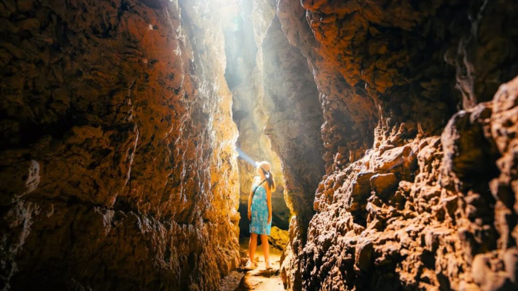visitor exploring inside a narrow cave corridor with textured limestone walls