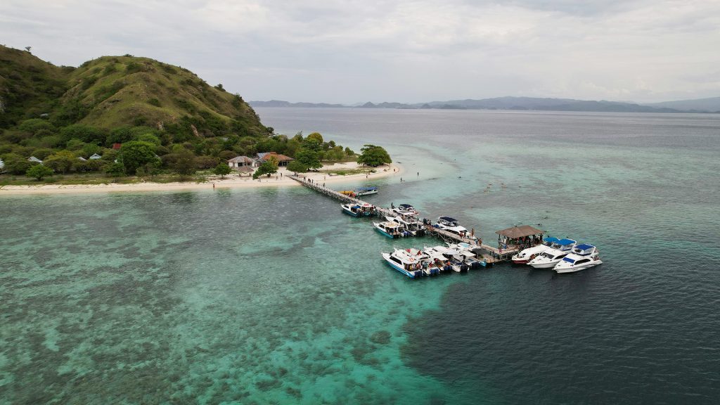 Boats docked at Kanawa Island pier with calm sea and clear water during dry season in Labuan Bajo