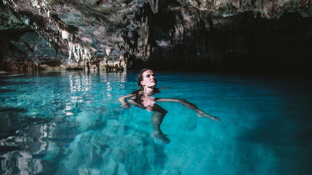 woman swimming in a natural cave pool with rock formations and clear water