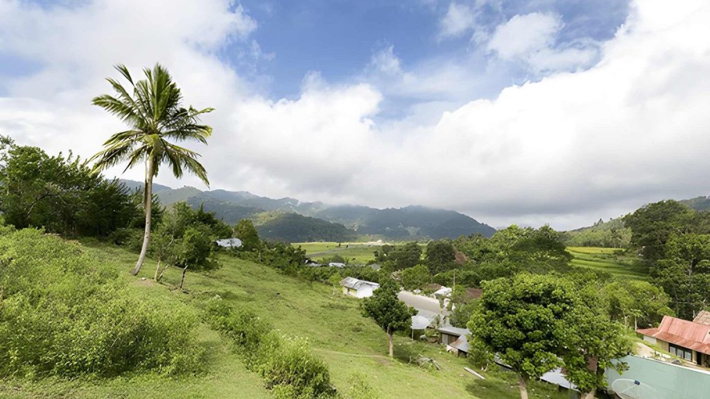 hillside view of Moni Village with tropical trees and mountain backdrop in Flores Indonesia